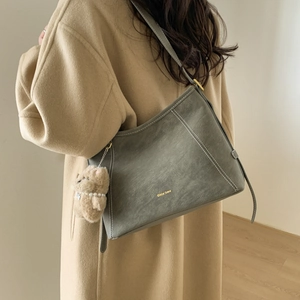 Detail of sage green leather bag with white contrast stitching and cute plush bear charm