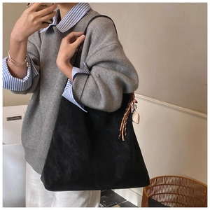 Detail view of large black suede tote bag featuring ethnic woven knot and heart charm