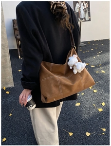 Détail d'un sac cabas marron avec surpiqûres blanches et pendentif de chiot en peluche