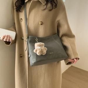 Detail of grey crossbody bag with white stitching, gold logo, and a plush bear charm