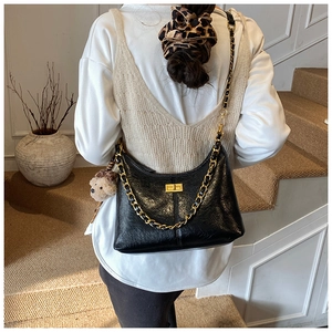 Detail of black glossy crescent bag with gold chain strap and cute bear charm pendant
