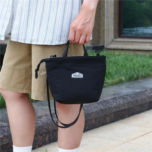 Detail of a black nylon drawstring bag with dual handles and crossbody strap in use