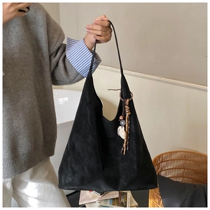 Detail view of large black suede tote bag with ethnic tassel charm and floral accents