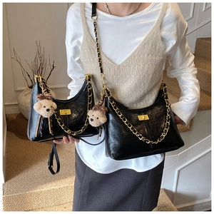 Close-up of black quilted hobo bag with gold hardware and plush bear accessory