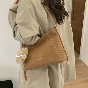 Detail of a brown shoulder bag featuring white contrast stitching and a cute plush bear charm