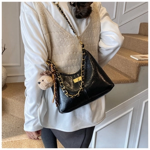Detail of black glossy quilted bag with gold chain strap and plush puppy charm