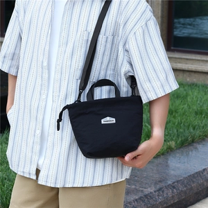 Outdoor view of a black lightweight nylon crossbody bag worn by a model in nature