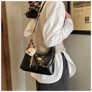 Close-up of black glossy hobo bag featuring bold gold chain and cute bear charm