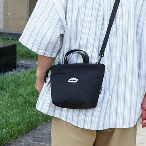 Outdoor lifestyle shot of a black nylon crossbody bag with drawstring closure on model