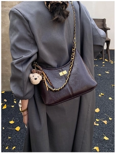 Detail of dark brown quilted chain bag featuring a plush bear charm on grey wool coat