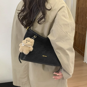 Detail of black vintage bucket bag featuring white contrast stitching and a cute bear charm