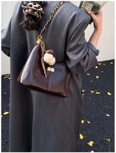 Close-up of hobo bag with gold twist lock, metal chain strap and white plush charm detail