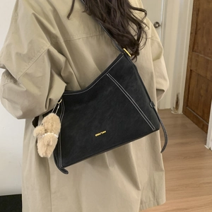 Detail view of retro black shoulder bag with white contrast stitching and a plush bear charm