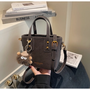 Detail of dark gray lychee leather handbag with gold logo and plush monster charm accessory