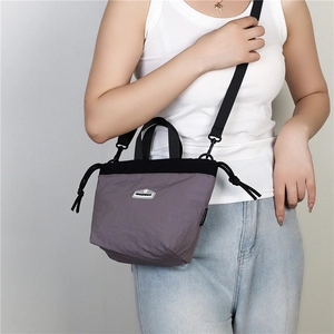 Detail of greyish-purple nylon crossbody bag with drawstring and brand logo patch
