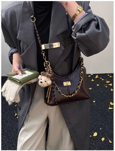 Detail of dark brown crescent bag with gold chain strap and teddy bear charm on model