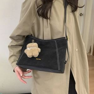 Detail of black suede shoulder bag with contrast stitching and teddy bear charm