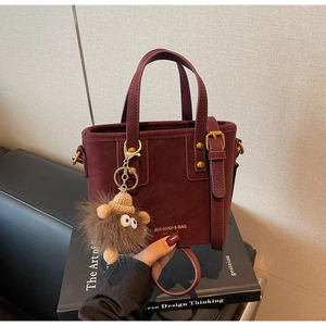 Detail of wine red bucket bag with gold buckle, faux leather texture, and plush charm