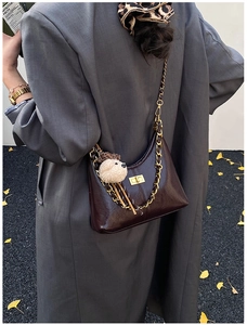Detail of dark brown glossy leather crescent bag with gold chain and plush dog charm