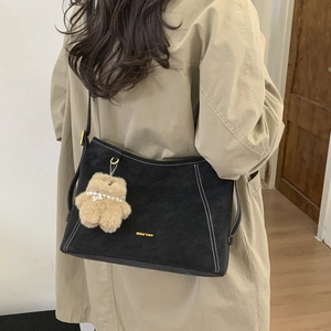 Close-up of black bucket bag with white contrast stitching and cute plush bear charm