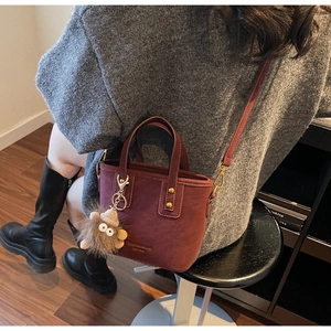 Detail of burgundy matte tote bag with plush charm and rivets on a shoulder strap