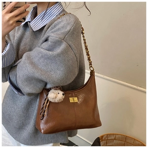 Close-up of brown quilted shoulder bag featuring gold chain strap and plush puppy charm