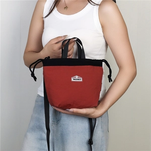 Detail of red and black nylon crossbody bag with drawstring closure and brand shield
