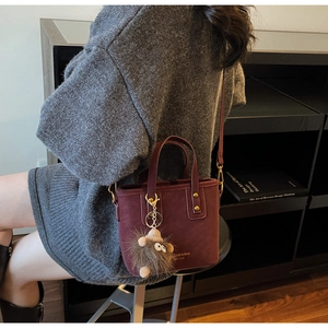 Detail of burgundy bucket bag with cute hedgehog charm worn over a grey knit dress