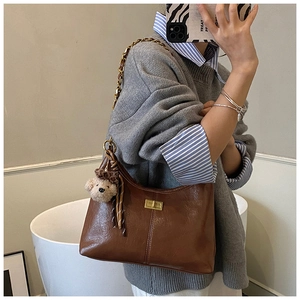 Detail of brown hobo bag with oil wax leather texture and gold chain strap and teddy charm