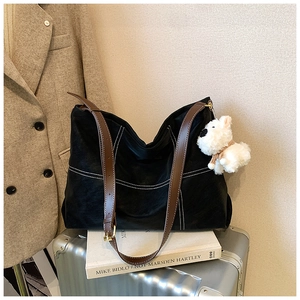 Détail du cabas en cuir noir avec coutures blanches et anses marrons sur des valises