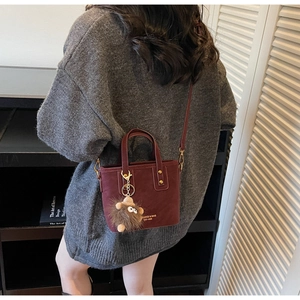 Detail of burgundy vintage crossbody bag with plush charm and golden logo on textured leather