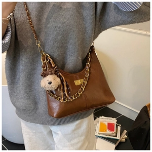 Detailed view of brown quilted crossbody bag featuring chain strap and plush bear charm