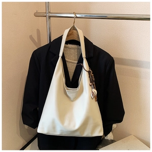 Detail of a beige faux leather tote bag with leaf pendant charm on a black blazer
