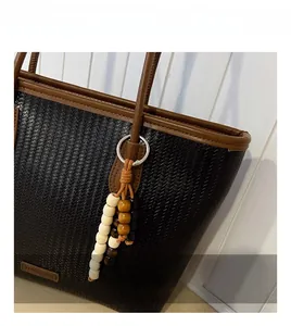 Detail of black woven tote bag featuring brown leather trim and multi-color beaded charm