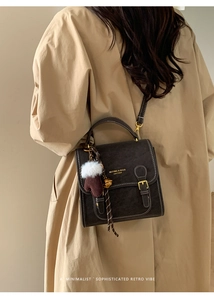 Detail der dunkelbraunen Retro-Schultertasche mit weißer Naht und Plüsch-Anhänger