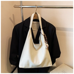 Detail of a creamy white leather hobo bag with ethnic tassel on a black blazer background