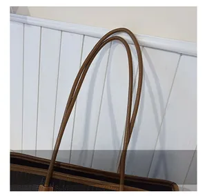 Detail showing the brown leather handle and black woven texture of the tote bag