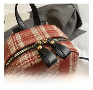 Detail showing the red plaid tweed fabric, dual gold zippers and black leather handle
