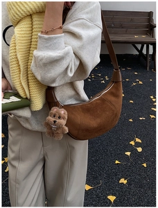 Close-up of caramel suede crescent shoulder bag featuring a cute plush dog pendant charm