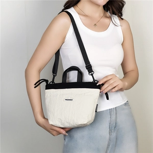 Detail of a lightweight nylon crossbody bag in beige and black with a branded patch