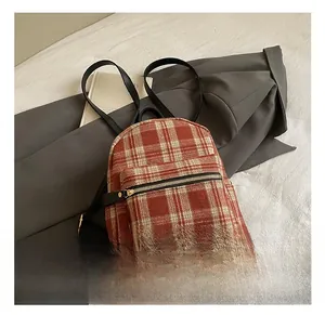 Detail showing red and beige plaid pattern backpack with black leather straps and gold zipper
