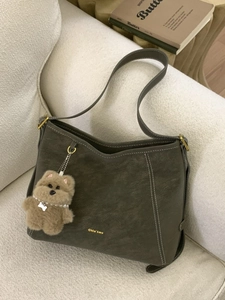 Olive green leather bucket bag with white stitching and plush bear charm on sofa