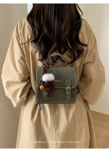 Detail eines dunkelgrünen Retro-Lederrucksacks mit Winteranhänger auf einem Trenchcoat