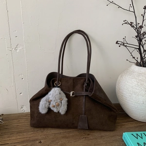 Detail of dark brown matte leather tote bag with grey plush bunny charm on wooden table