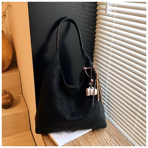 Artistic detail of a black suede hobo tote bag featuring a coffee cup charm in light shadow