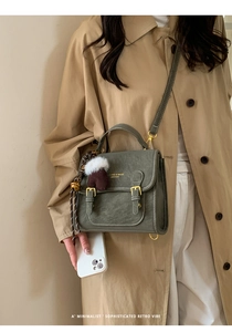 Detail der olivgrauen Vintage-Umhängetasche mit Doppelschnallen und Handschuh-Anhänger