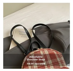 Close-up of red plaid backpack featuring black leather adjustable straps and top handle