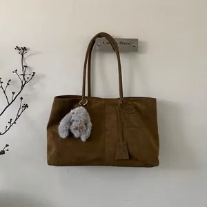 Detail einer braunen matten Tragetasche mit Plüschhasen-Anhänger an einer Wand