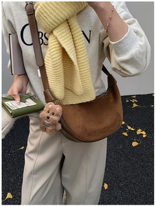Detail of a brown suede crescent bag with a plush dog charm in an autumn outdoor setting
