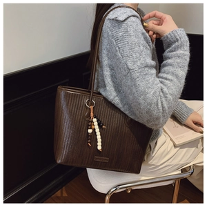 Detail of dark brown woven tote bag featuring a decorative beaded tassel on the strap